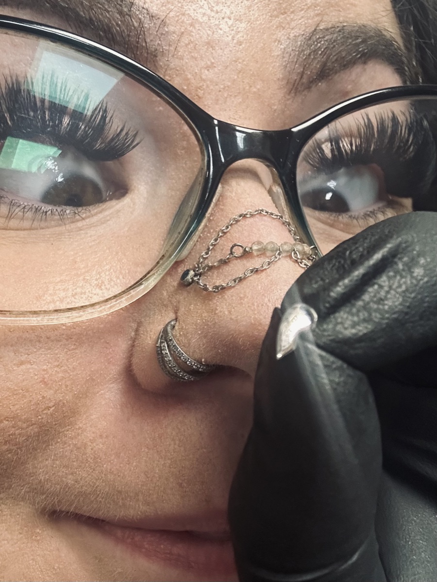 Sairuh MacKay, owner of Lumen Piercing, in a close-up selfie with her nostril and bridge-chain jewelry
